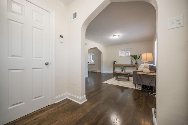 corridor featuring arched walkways, wood finished floors, visible vents, and baseboards