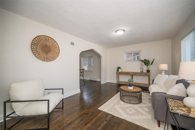 sitting room with arched walkways, a wealth of natural light, visible vents, wood finished floors, and baseboards