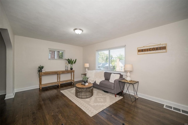 living area with arched walkways, wood finished floors, visible vents, and baseboards