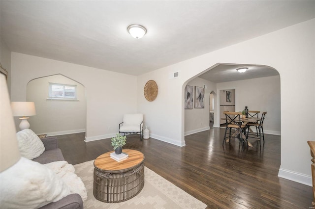 living area with arched walkways, wood finished floors, visible vents, and baseboards