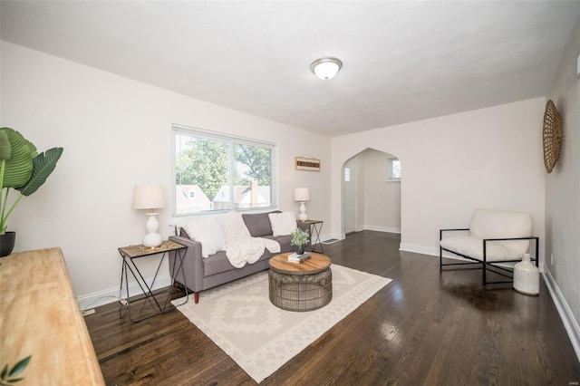 living room featuring dark wood-type flooring, arched walkways, and baseboards