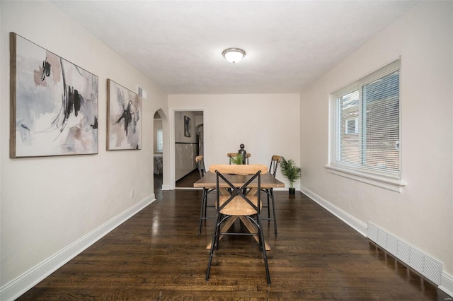 dining space with dark wood-style floors, baseboards, visible vents, and arched walkways