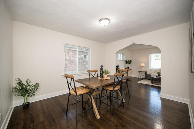 dining room with arched walkways, wood finished floors, and baseboards