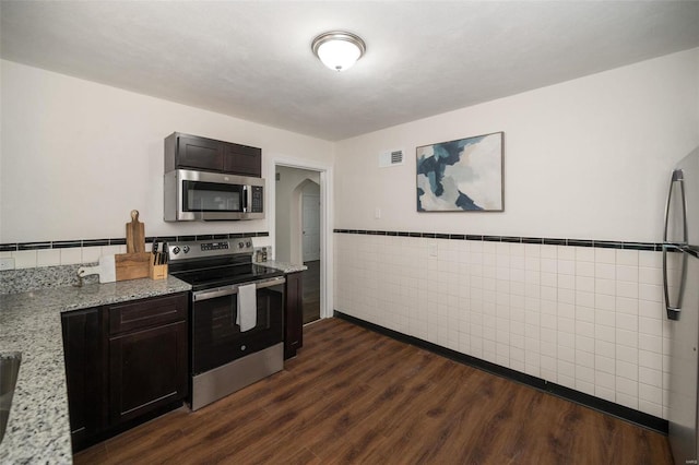 kitchen with arched walkways, visible vents, appliances with stainless steel finishes, light stone countertops, and dark wood finished floors