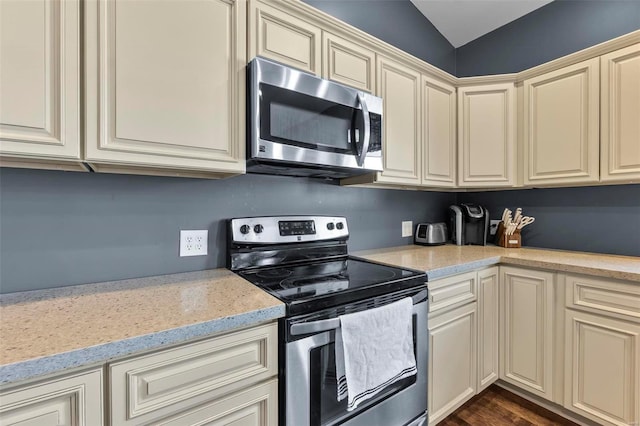 kitchen featuring light stone counters, appliances with stainless steel finishes, dark wood finished floors, and cream cabinetry