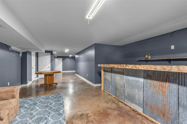 bar featuring baseboards, a bar, and finished concrete floors