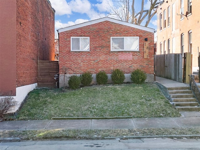 view of home's exterior featuring brick siding, fence, and a lawn