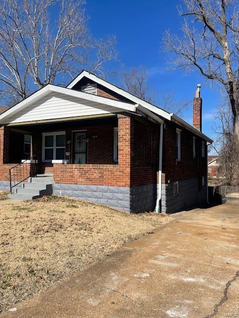 view of side of property with covered porch, brick siding, and a chimney