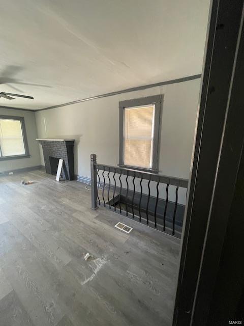 unfurnished living room with wood finished floors, visible vents, baseboards, a ceiling fan, and a brick fireplace