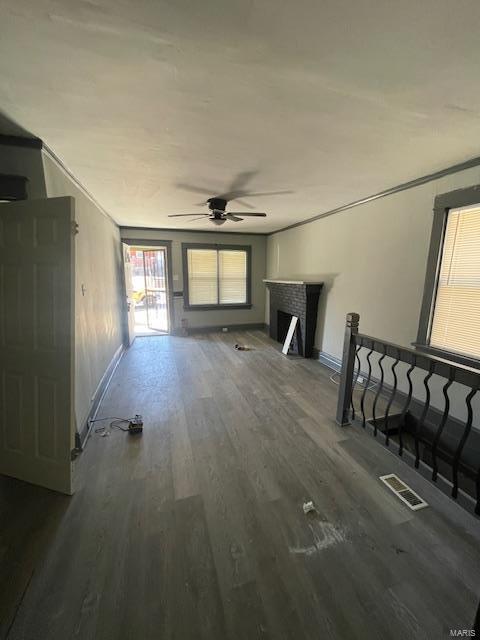 unfurnished living room with a fireplace, wood finished floors, visible vents, baseboards, and a ceiling fan