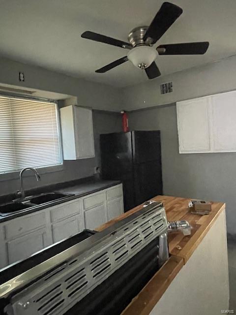 kitchen featuring visible vents, a sink, freestanding refrigerator, and white cabinets