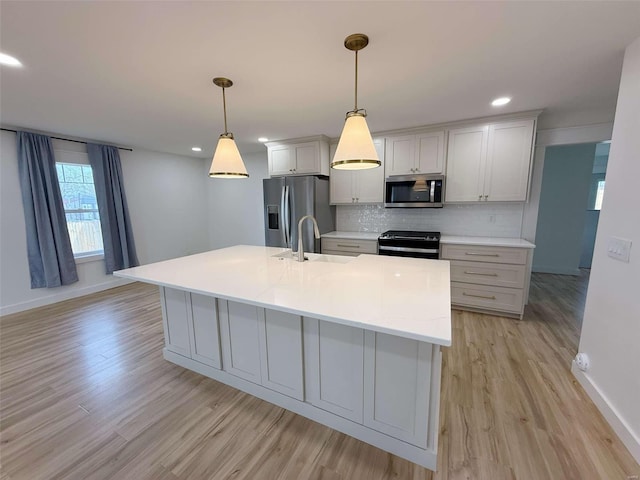 kitchen with a sink, appliances with stainless steel finishes, light wood-type flooring, decorative backsplash, and a center island with sink