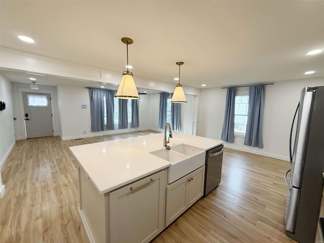 kitchen with appliances with stainless steel finishes, hanging light fixtures, light countertops, light wood-style floors, and a sink