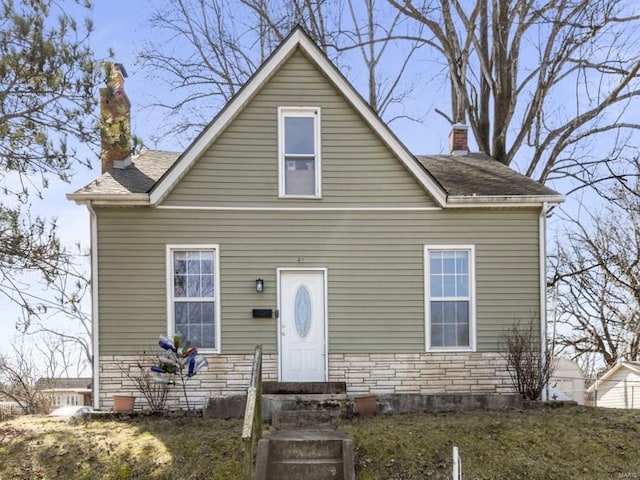 bungalow featuring stone siding, a shingled roof, and a chimney