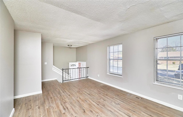 empty room with visible vents, a textured ceiling, baseboards, and wood finished floors