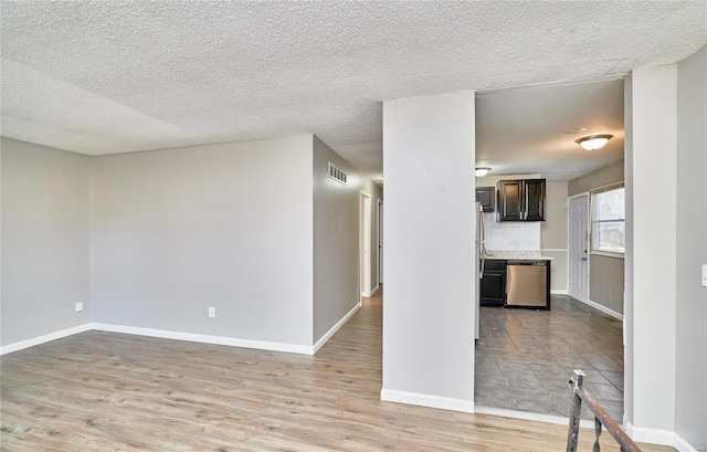 interior space featuring a textured ceiling, light wood-style flooring, visible vents, and baseboards