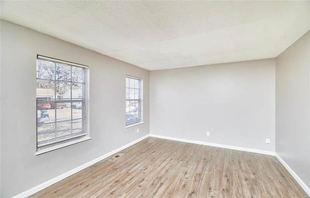 empty room with visible vents, a textured ceiling, baseboards, and wood finished floors