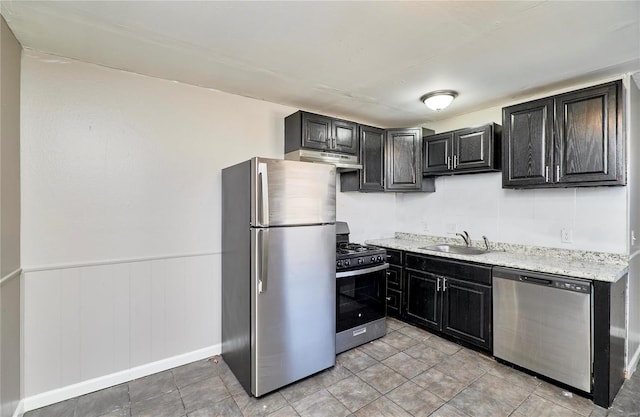 kitchen with wainscoting, appliances with stainless steel finishes, dark cabinetry, under cabinet range hood, and a sink