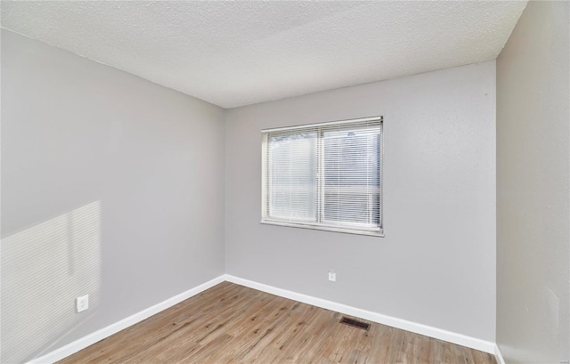 empty room with a textured ceiling, wood finished floors, visible vents, and baseboards