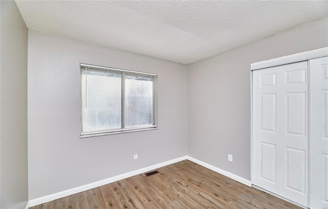 unfurnished bedroom with baseboards, visible vents, wood finished floors, a textured ceiling, and a closet