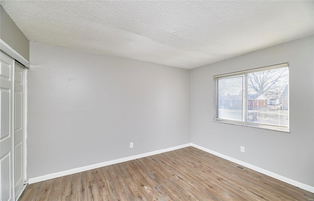 empty room with visible vents, a textured ceiling, baseboards, and wood finished floors