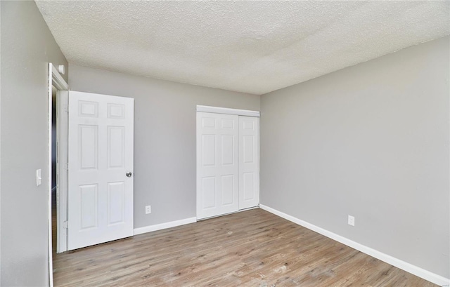 unfurnished bedroom with a textured ceiling, a closet, baseboards, and wood finished floors