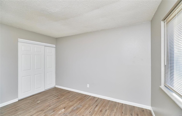 unfurnished bedroom with a textured ceiling, a closet, wood finished floors, and baseboards