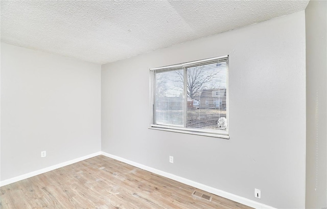 unfurnished room with visible vents, a textured ceiling, baseboards, and wood finished floors