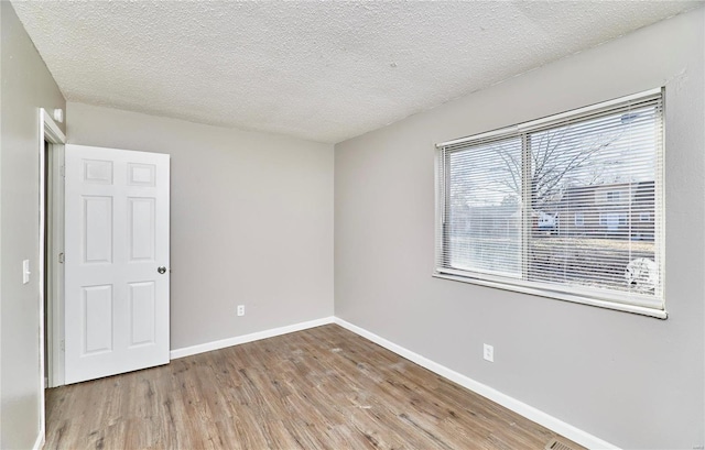 spare room with a textured ceiling, wood finished floors, and baseboards