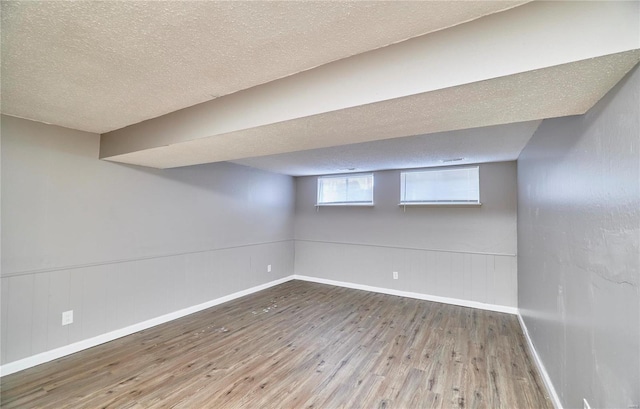 basement with a textured ceiling, hardwood / wood-style floors, wainscoting, and baseboards