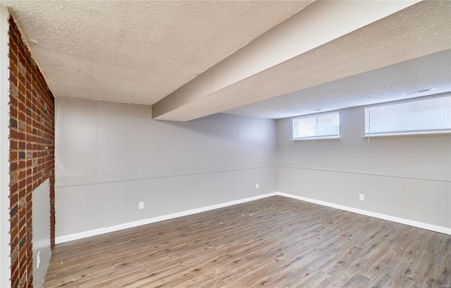 basement with a textured ceiling, wainscoting, wood finished floors, and baseboards