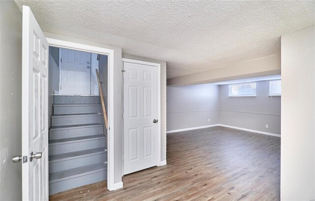 staircase featuring a textured ceiling, wood finished floors, and baseboards