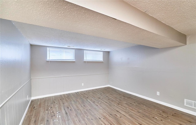 below grade area featuring a textured ceiling, a wainscoted wall, wood finished floors, visible vents, and baseboards