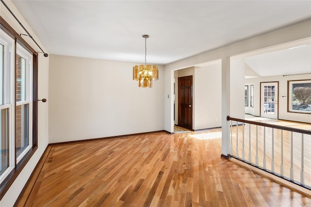 spare room with light wood-style floors, a notable chandelier, baseboards, and a wealth of natural light