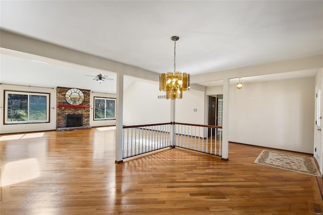 spare room with baseboards, visible vents, wood finished floors, a fireplace, and ceiling fan with notable chandelier