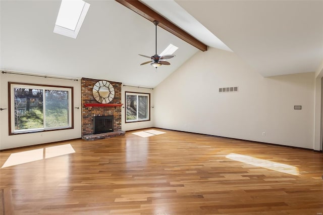 unfurnished living room featuring a skylight, beam ceiling, visible vents, a brick fireplace, and ceiling fan