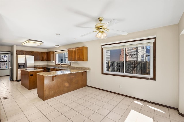 kitchen with light stone counters, a center island, baseboards, a peninsula, and stainless steel fridge with ice dispenser