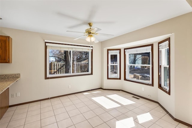 empty room with a healthy amount of sunlight, light tile patterned floors, ceiling fan, and baseboards