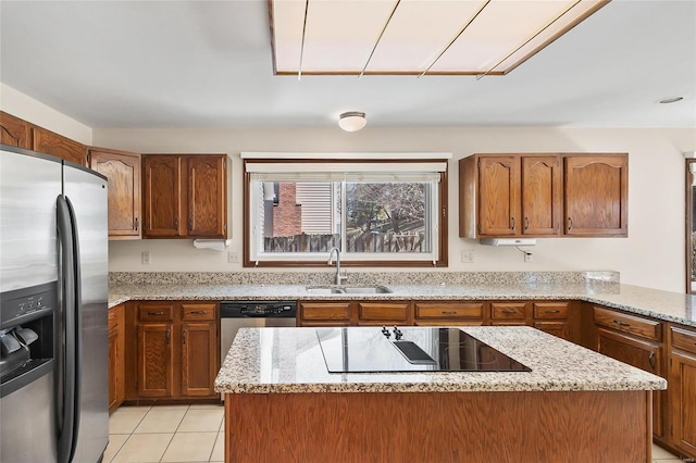 kitchen with appliances with stainless steel finishes, brown cabinetry, a sink, and light stone countertops