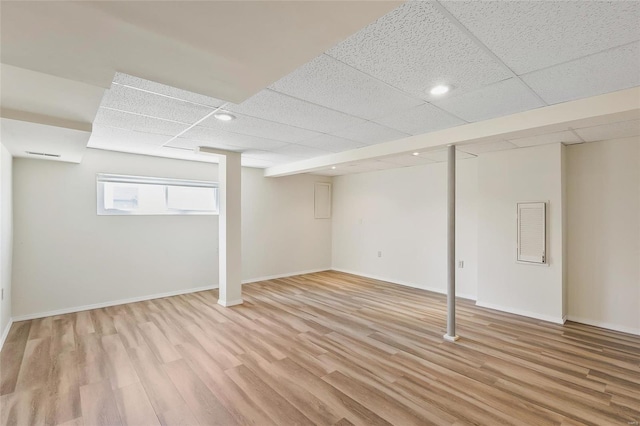 basement with a paneled ceiling, light wood-style floors, and baseboards