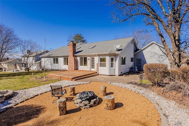 rear view of property featuring an outdoor fire pit, a chimney, a wooden deck, and a lawn