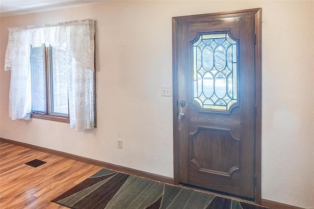 entryway with baseboards, wood finished floors, visible vents, and a healthy amount of sunlight