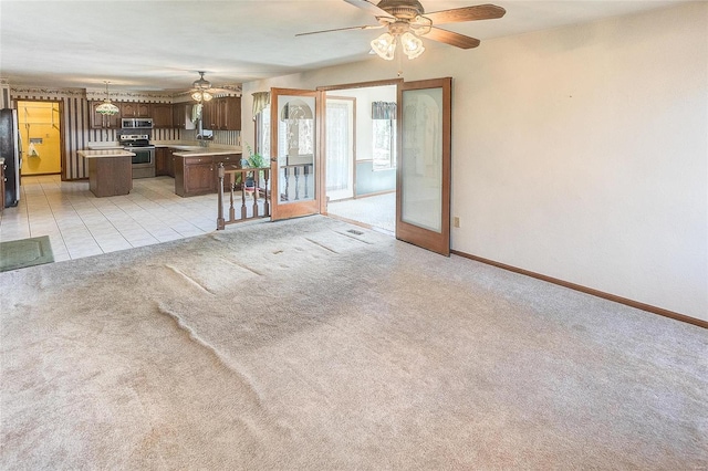 interior space with light tile patterned flooring, ceiling fan, baseboards, and light colored carpet