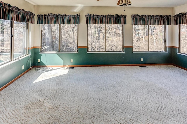 carpeted empty room with baseboards, visible vents, and a ceiling fan