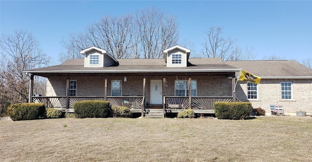 view of front of home featuring a front lawn, covered porch, brick siding, and roof with shingles