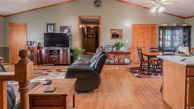 living room with a wainscoted wall, light wood finished floors, lofted ceiling, ceiling fan, and ornamental molding