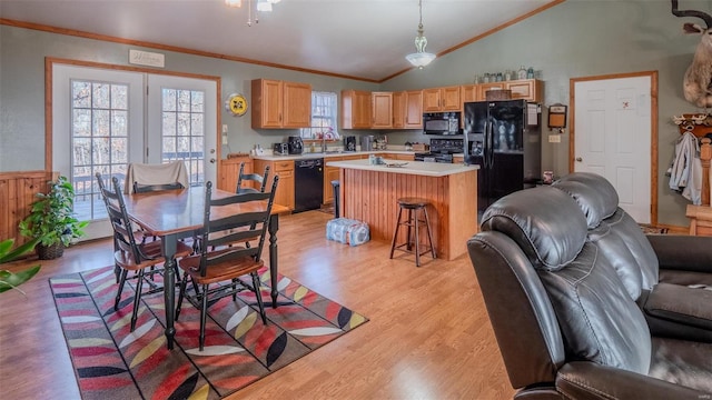 kitchen with light wood finished floors, a sink, black appliances, vaulted ceiling, and light countertops