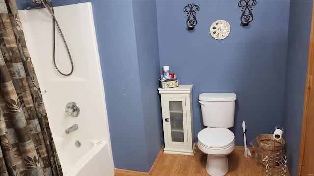 bathroom with shower / bath combo with shower curtain, toilet, wood finished floors, and baseboards