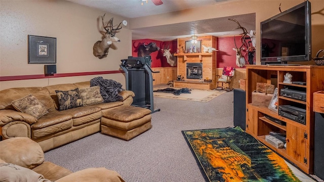 living area with a wainscoted wall, a fireplace, ceiling fan, wood walls, and carpet flooring