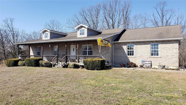 view of front facade with brick siding, a porch, a shingled roof, and a front yard